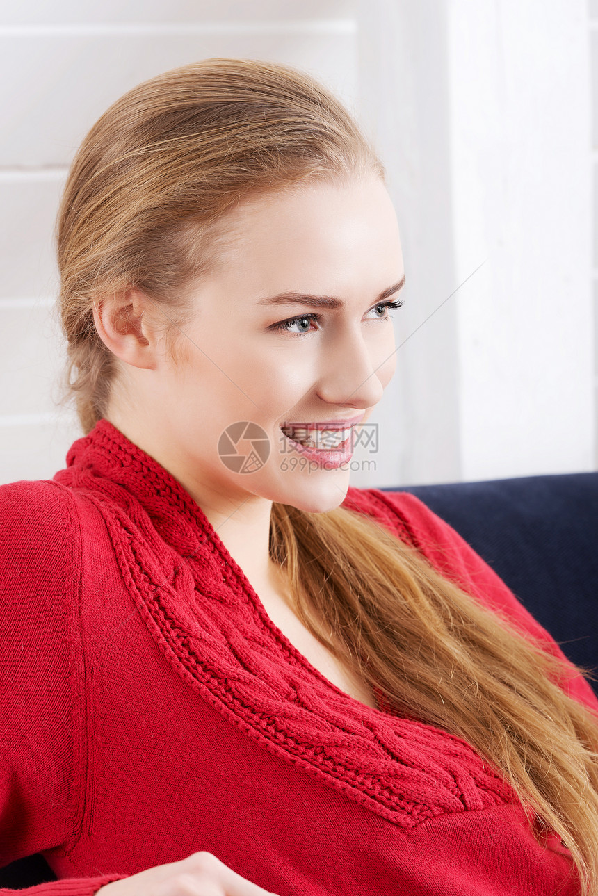 美丽的caucasian女人坐在沙发上 穿着红色拉风服衣服青少年休息感情亲热闲暇女孩女儿沉思毛衣图片