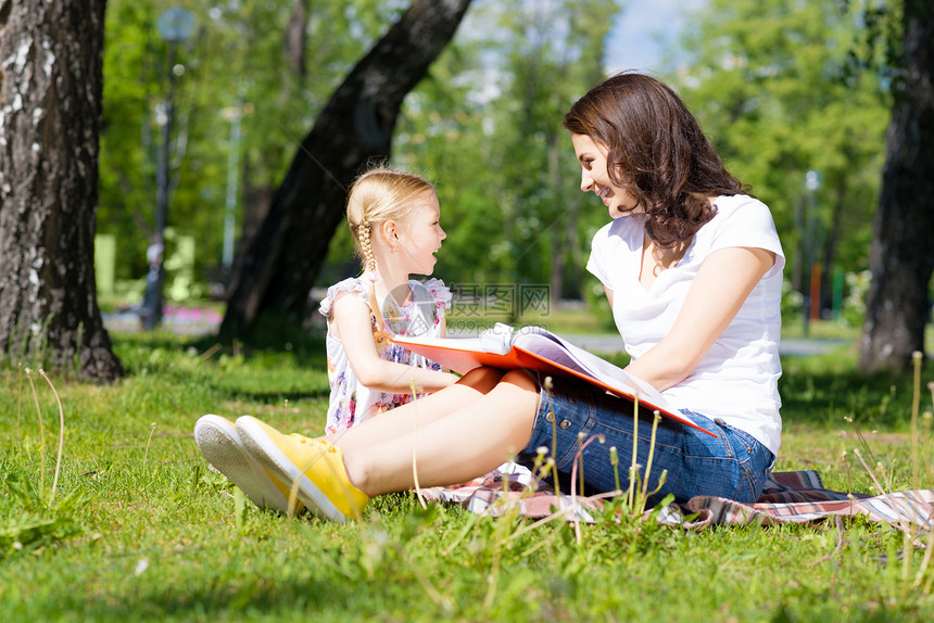 女孩和年轻女子一起阅读一本书绘画老师托儿所成人公园快乐后院场地学习女士图片