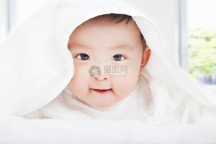 在白色毛毯或毛巾下微笑的婴儿图片