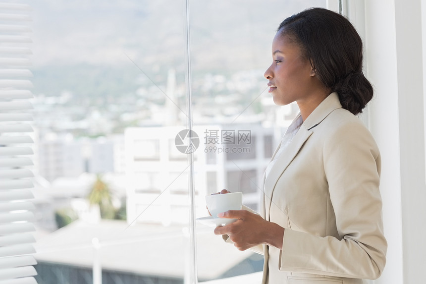 有茶杯的优美女商务人士 透过办公室窗户看图片
