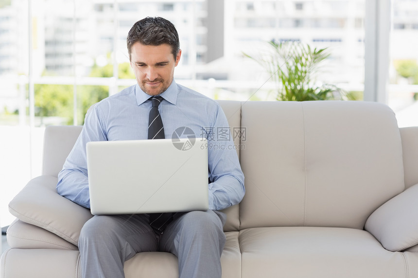 在家使用笔记本电脑的穿衣人领带房子男人裤子衬衫男性棕色办公长椅家庭生活图片