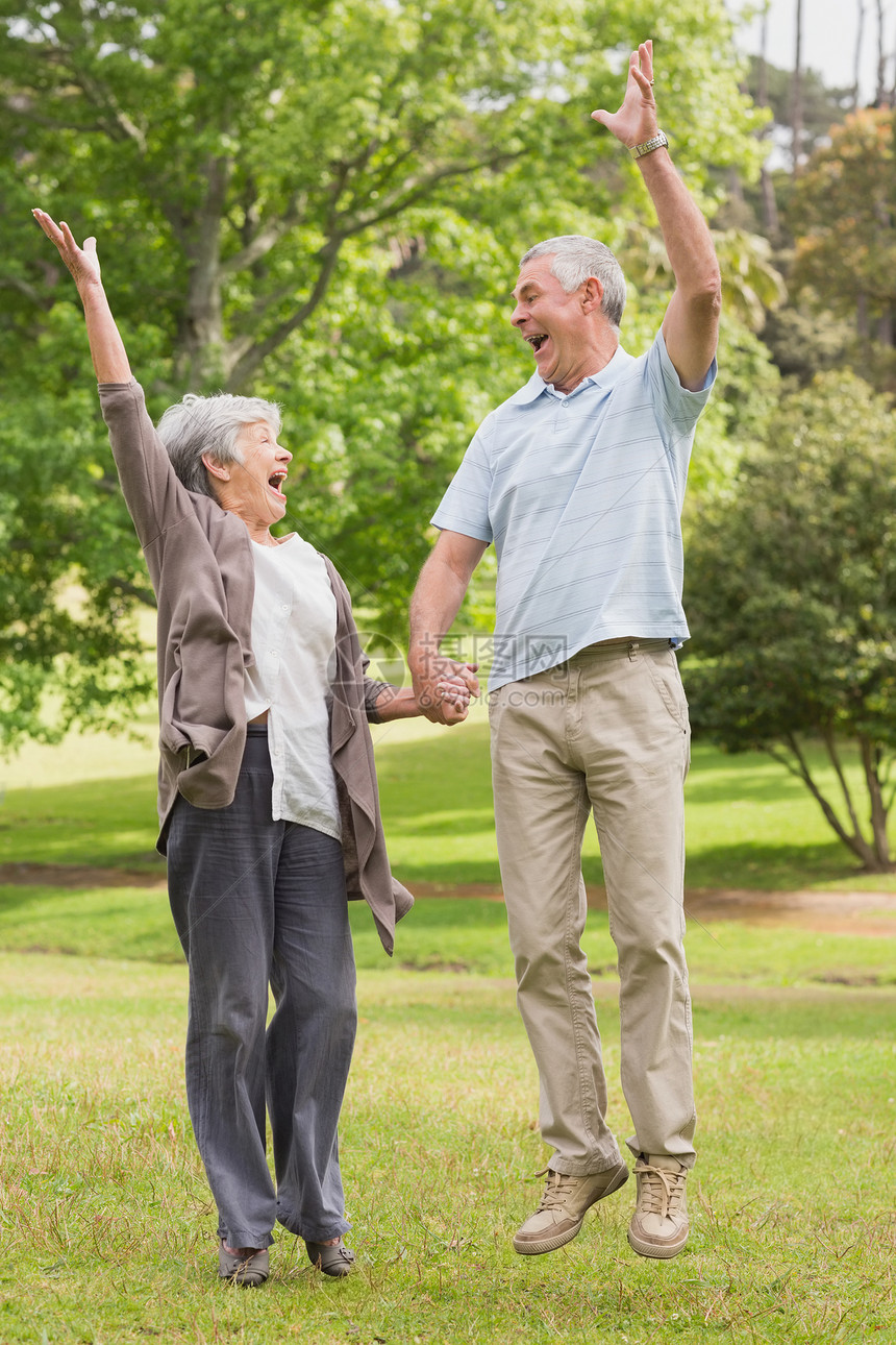 活跃的老年夫妇握手在公园跳跃图片