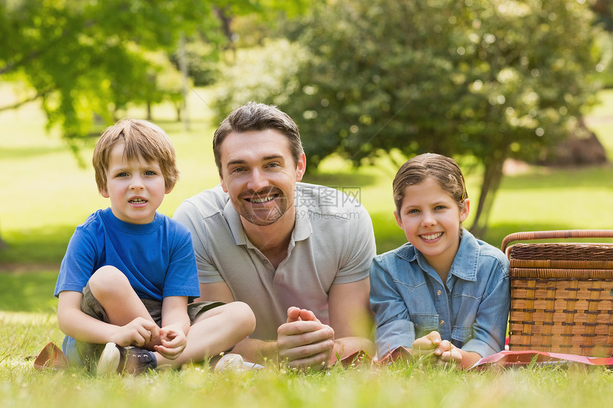 微笑的父亲与年轻的孩子 在公园的草地上躺在草地上图片