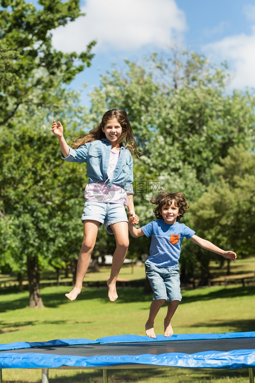 快乐的男孩女孩跳高在公园的蹦床上图片