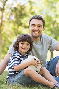 父亲和儿子 橄榄球坐在草地上背景图片