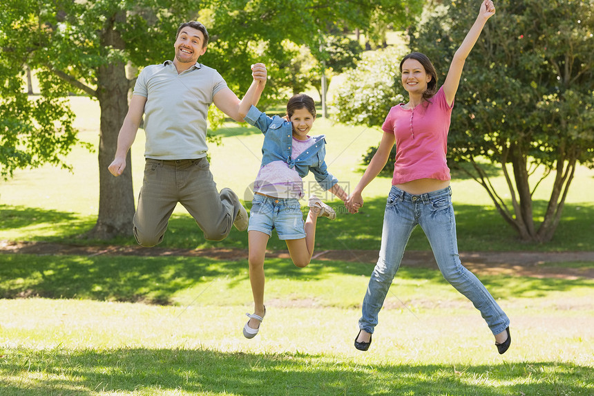 三个人一家三口手握手 在公园跳跃女孩闲暇女士男性男人女性微笑父亲绿地团结图片