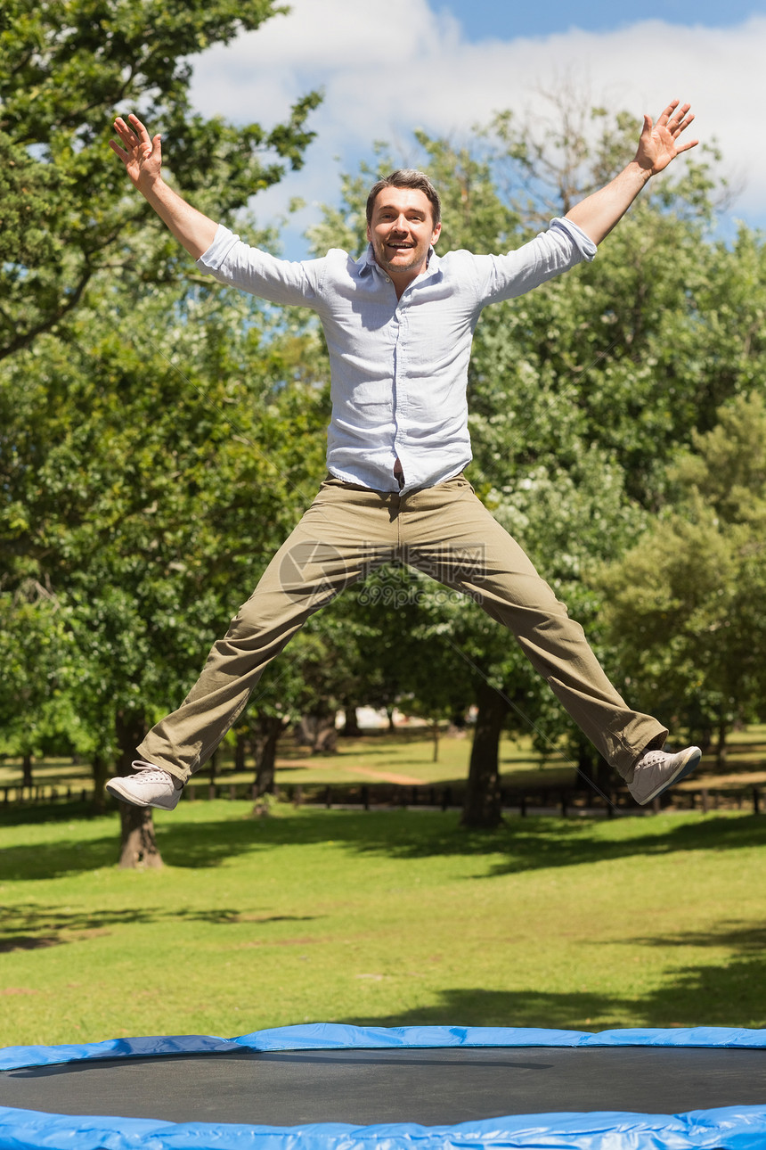 快乐的男人在公园的蹦床上跳高图片