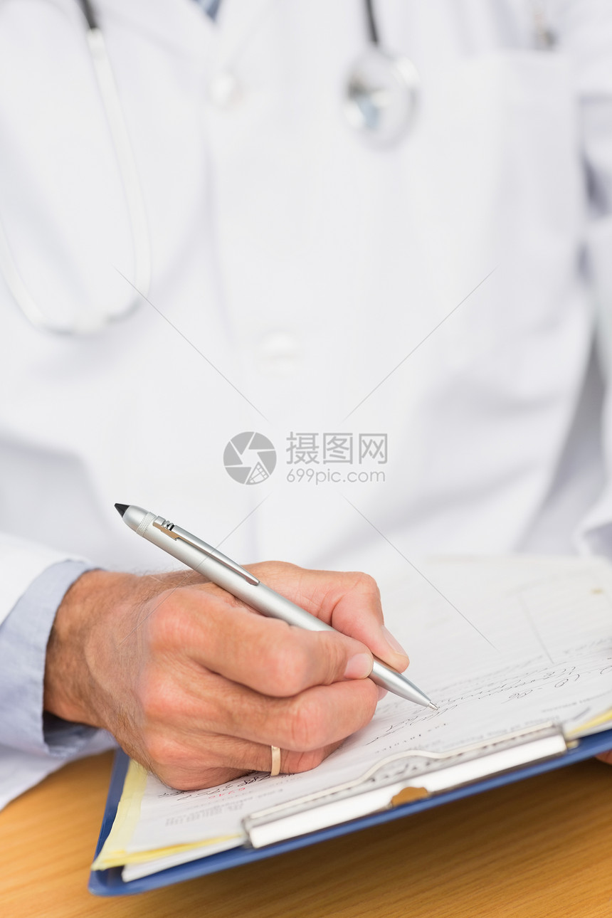 医生坐在桌子上写剪贴板诊所医疗医疗保健医务室从业者医师男性保健写作服务图片