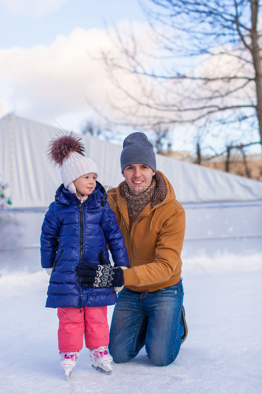 年轻父亲和可爱的小女孩 在滑冰场上童年帮助学习溜冰场滑冰乐趣训练孩子手套数字图片