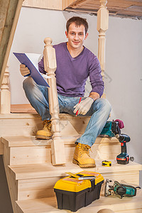 青年木匠坐在梯子的阶梯上 带工具背景图片