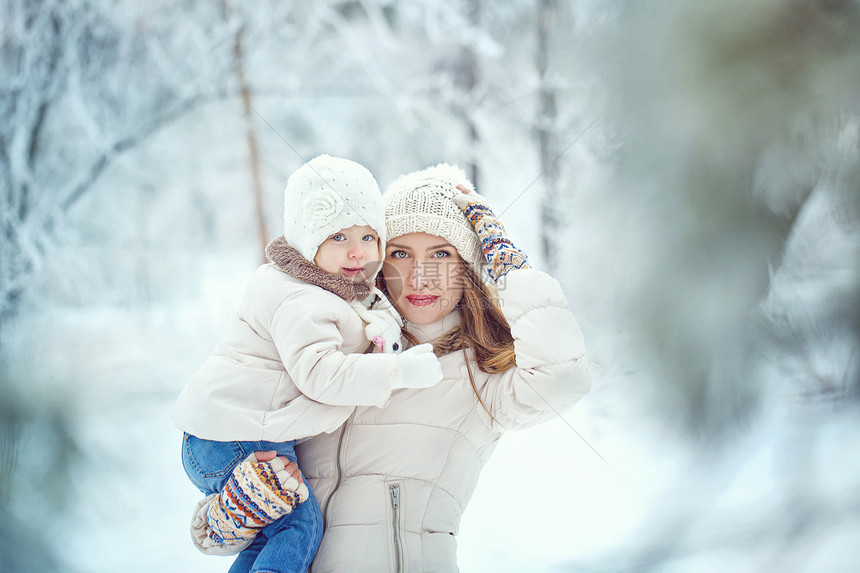 母亲在冬季森林里手握着女儿妈妈们童年女性幸福喜悦树木微笑女孩们帽子城市图片