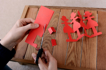 用剪刀剪断一连串红纸娃娃背景图片