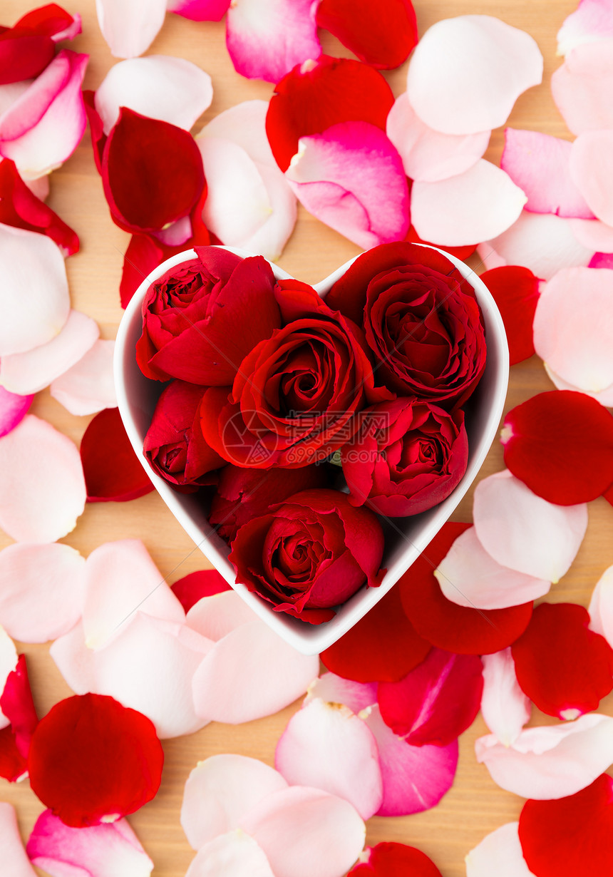 红玫瑰在心脏形状的碗里 旁边有粉红色花瓣图片