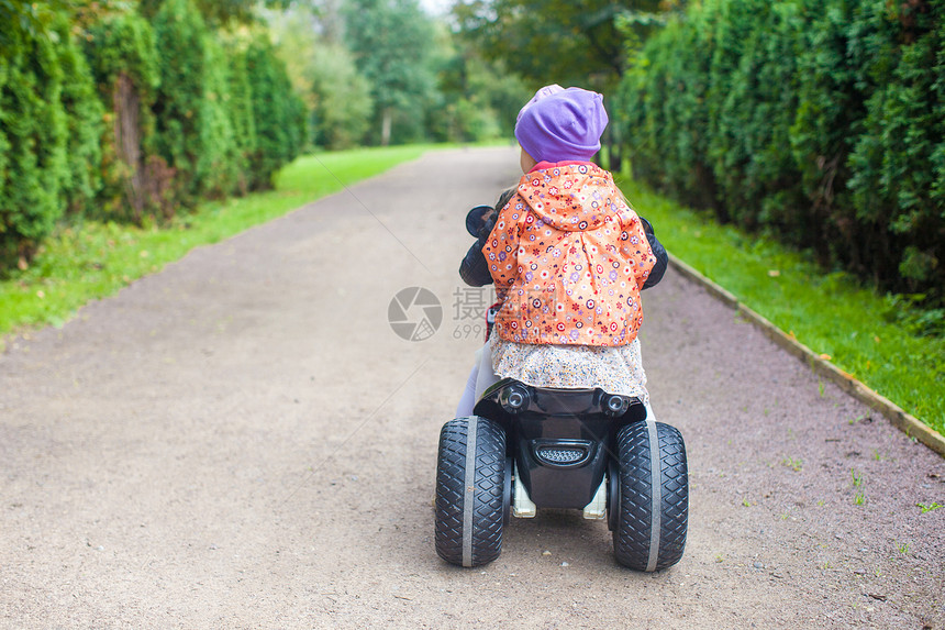 在绿公园骑摩托车的 可爱小女孩背面景色裙子婴儿童年公园速度运动晴天玩具孩子微笑图片
