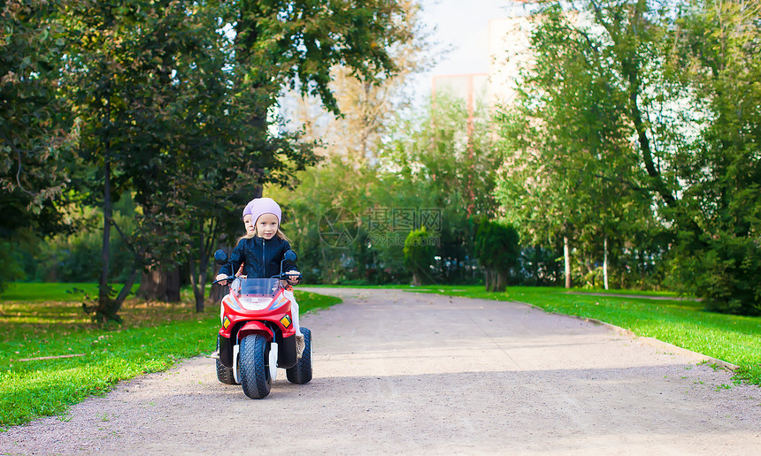 可爱的小女孩 在绿色公园骑着孩子的摩托车乐趣夹克快乐运动裙子童年公园游戏玩具姐姐图片