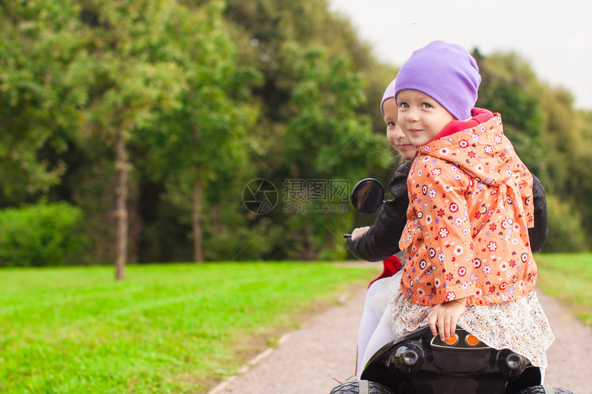 在绿色公园骑摩托车的可爱小女孩肖像 在绿色公园中女孩玩具活动裙子乐趣婴儿微笑公园速度运输图片