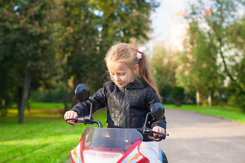 穿着皮夹克的可爱快乐的小姑娘 坐在玩具摩托车上晴天娱乐姐姐速度阳光孩子幼儿园女孩喜悦游戏图片