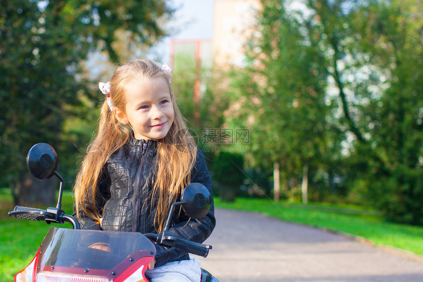 穿着皮夹克的小可爱摇滚女孩的肖像 坐在玩具摩托车上坐着引擎晴天喜悦娱乐阳光游戏幼儿园运动姐姐情感图片