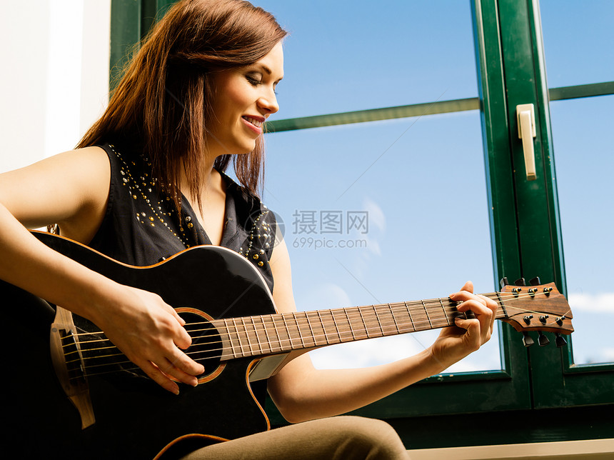 微笑的女人在窗边弹吉他图片