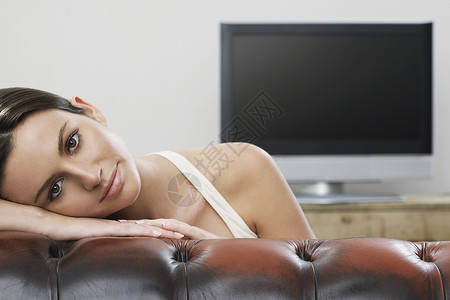 沙赫布雷特沙发上年轻女性在平板屏幕电视肖像前微笑摄影娱乐真皮女士成人黑发一人活动客厅背景