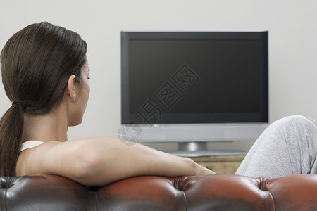 在沙发上看平板屏幕电视的年轻女青年高清图片