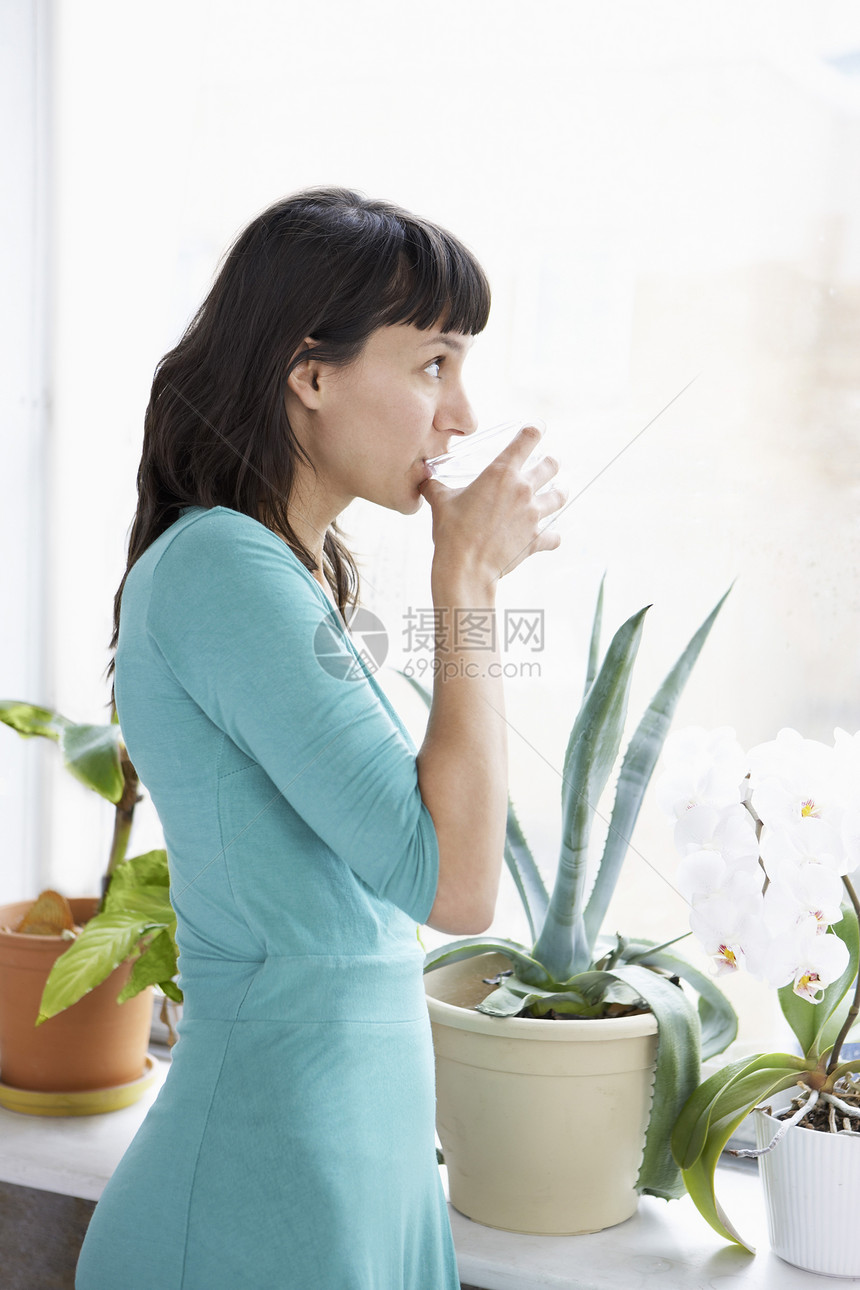 商业妇女饮酒和透过垃圾工厂的窗口看望图片