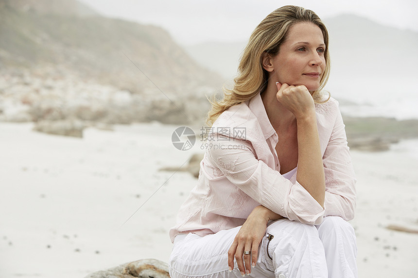 深思熟虑的下巴手在沙滩上坐在岩石上图片