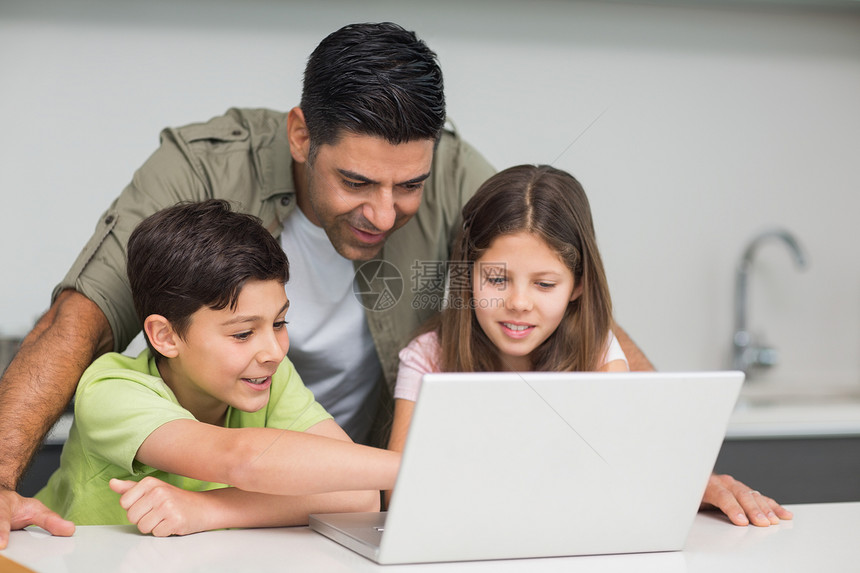 父亲有年幼的孩子在厨房用笔记本电脑房子学习兄弟闲暇女儿童年家庭互联网技术微笑图片