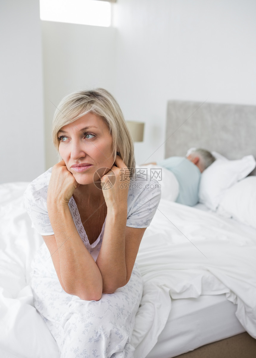 与背景男子一起坐在床上的十几岁的成年妇女睡眠夫妻思维家庭生活忧郁悲哀卧室女性愁云悲伤图片