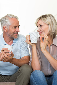 微笑的成年夫妇与咖啡杯坐在沙发上长椅房子杯子女性家庭生活客厅男性咖啡夫妻男人背景图片