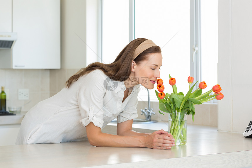 微笑的女人在厨房闻着鲜花的香味图片