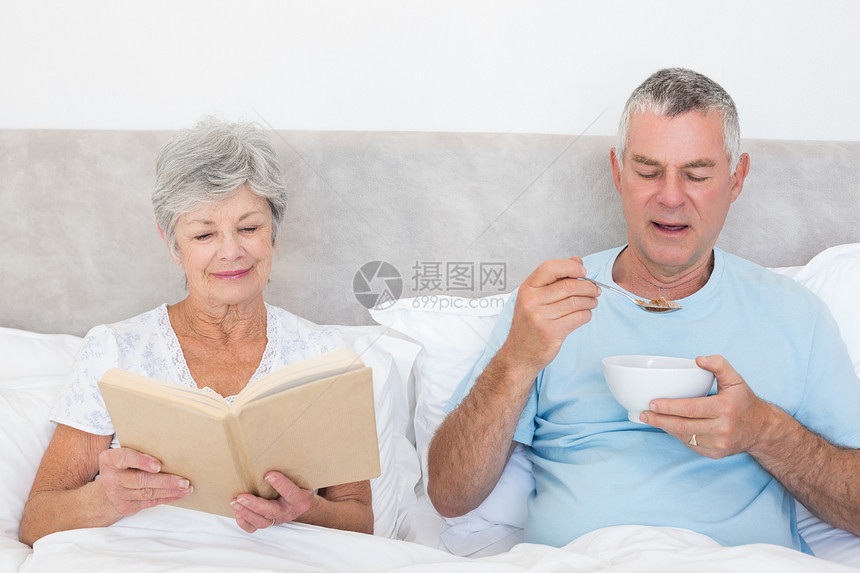 在床上有书和麦饭碗的老年夫妇图片