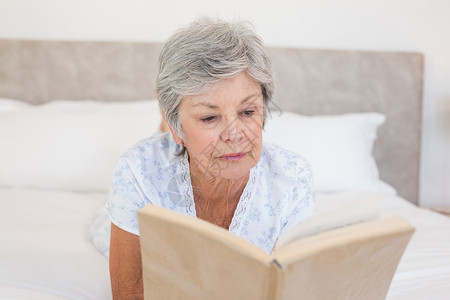 床上阅读故事书的老年妇女说谎白发爱好女性卧室房子岁月专注成人闲暇背景图片