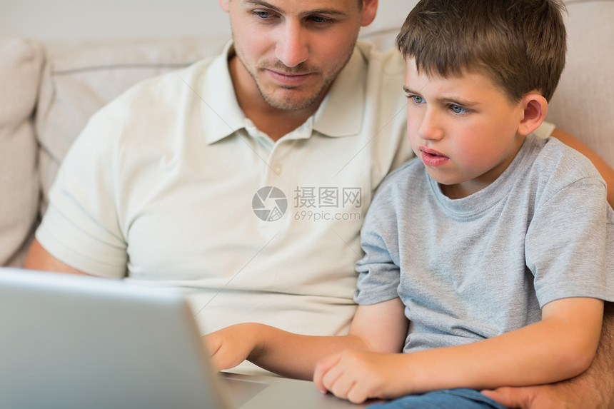 父亲和儿子在沙发上使用笔记本电脑家庭男性客厅孩子男生房子技术长椅男人便服图片