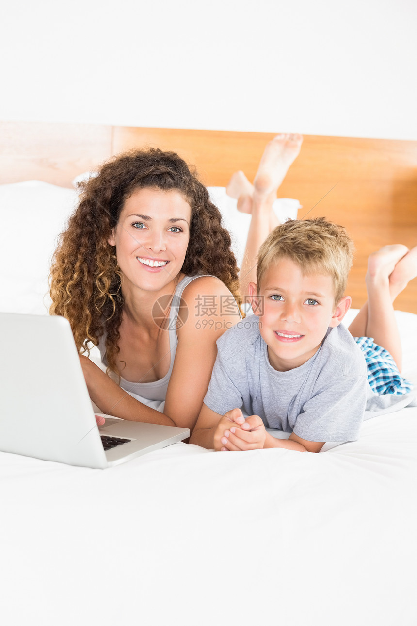 使用笔记本电脑躺在床上的金发美女男孩和母亲图片