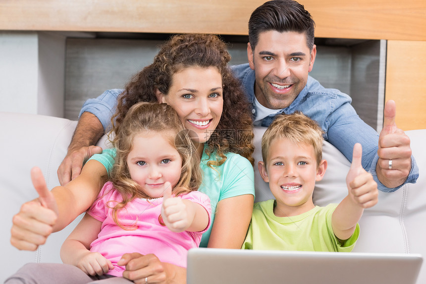幸福的家庭坐在沙发上 用笔记本电脑举起拇指图片