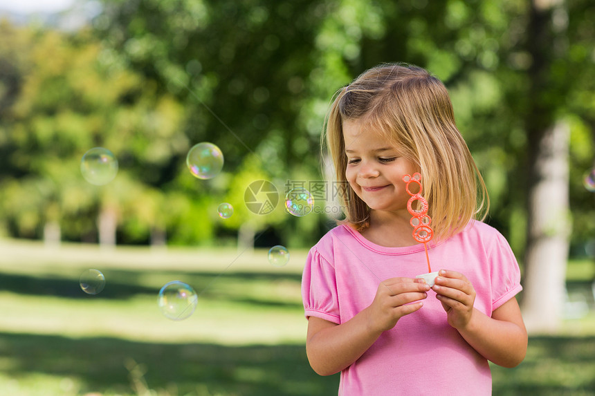 在公园吹肥皂泡的可爱女孩花园闲暇气泡浅色俏皮金发女郎自由粉色树木乐趣图片