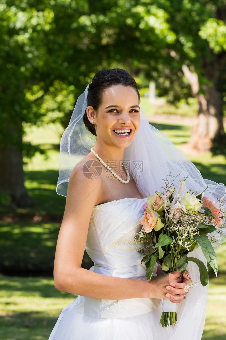 微笑美丽的新娘 用花束站在公园里图片