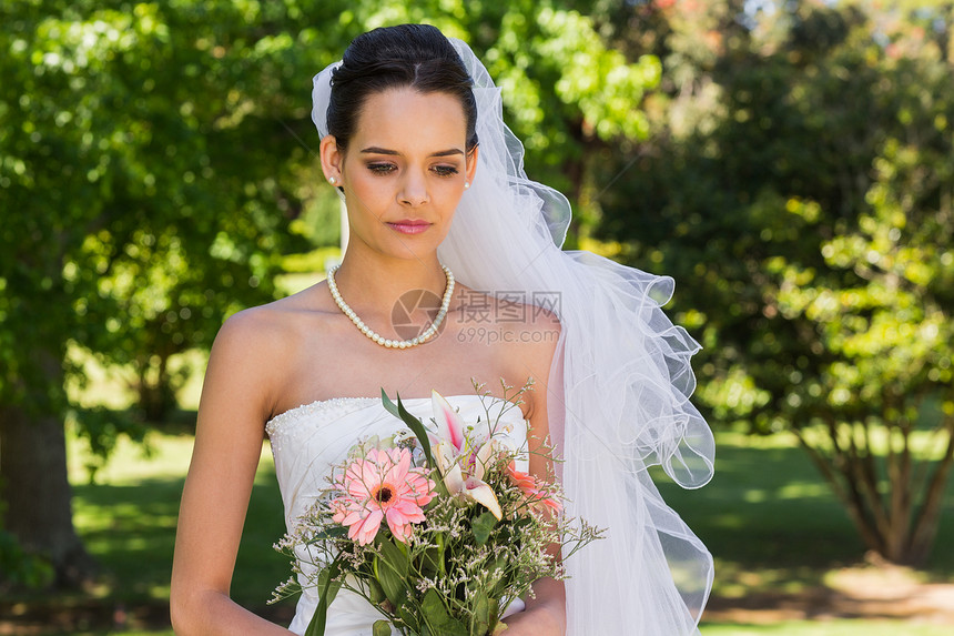 在公园里带花束的 美丽新娘婚姻婚纱草地面纱女士项链已婚树木婚礼珍珠图片