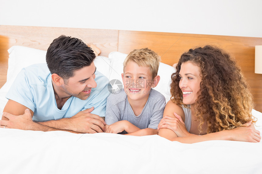 幸福的年轻家庭躺在床上互相看着对方图片
