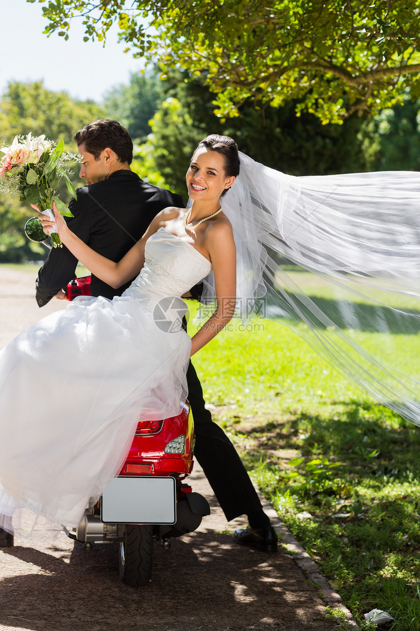 新婚夫妇坐在公园的摩托车上男人面纱新人幸福婚礼女士草地新郎运输微笑图片