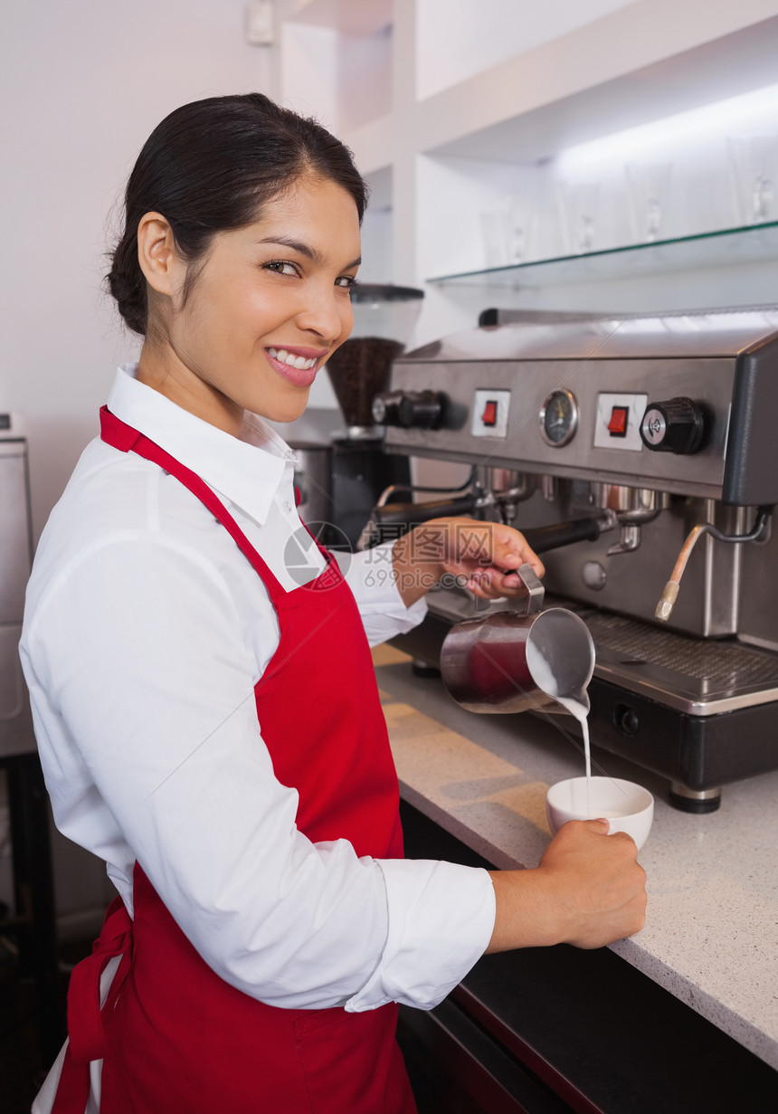把牛奶倒进咖啡杯的 漂亮的酒吧快乐行业职员咖啡微笑器具混血咖啡机职业饮料图片