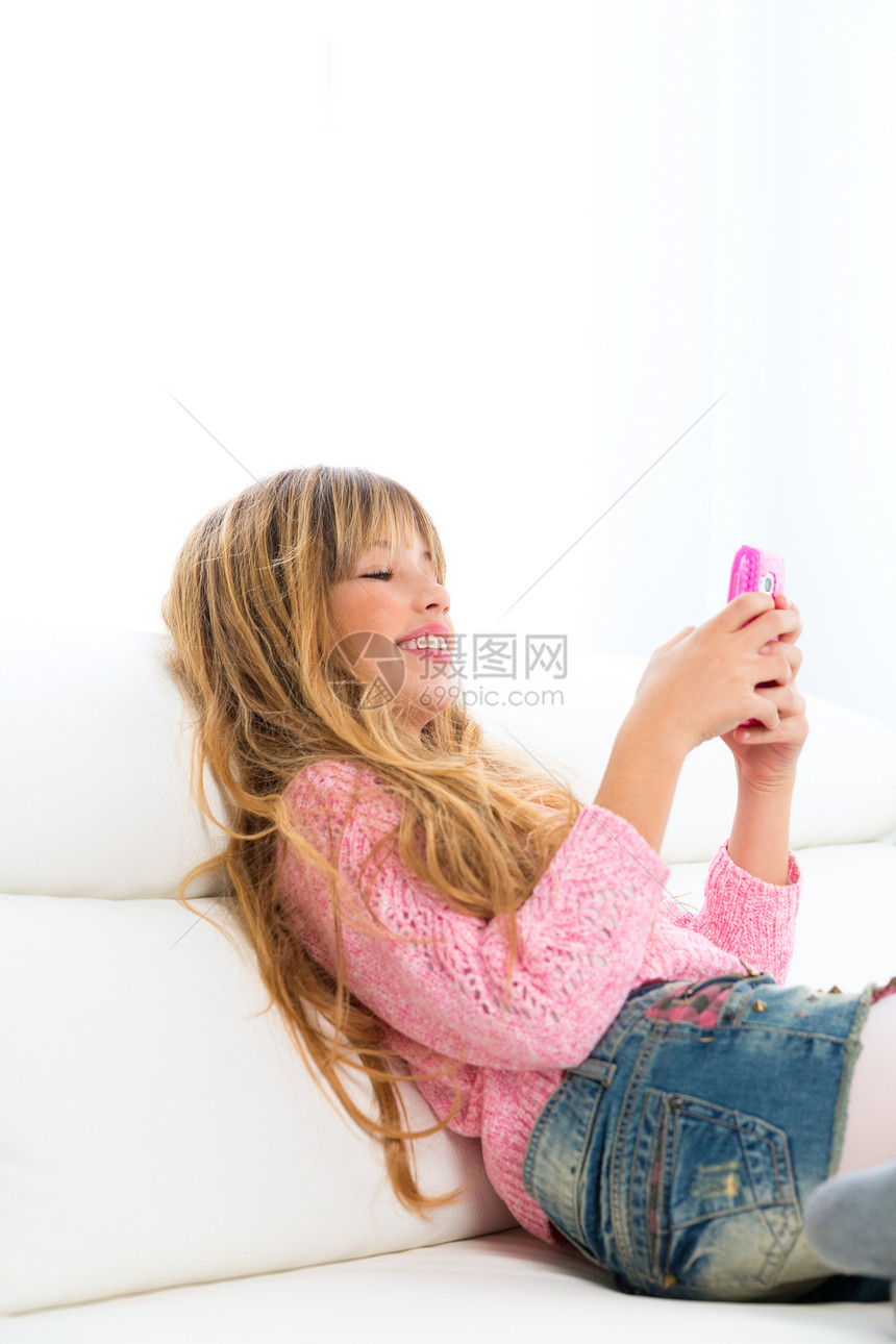 在白色沙发上用手机玩游戏的金子女孩互联网微笑技术孩子金发电子邮件女性童年享受牛仔裤图片