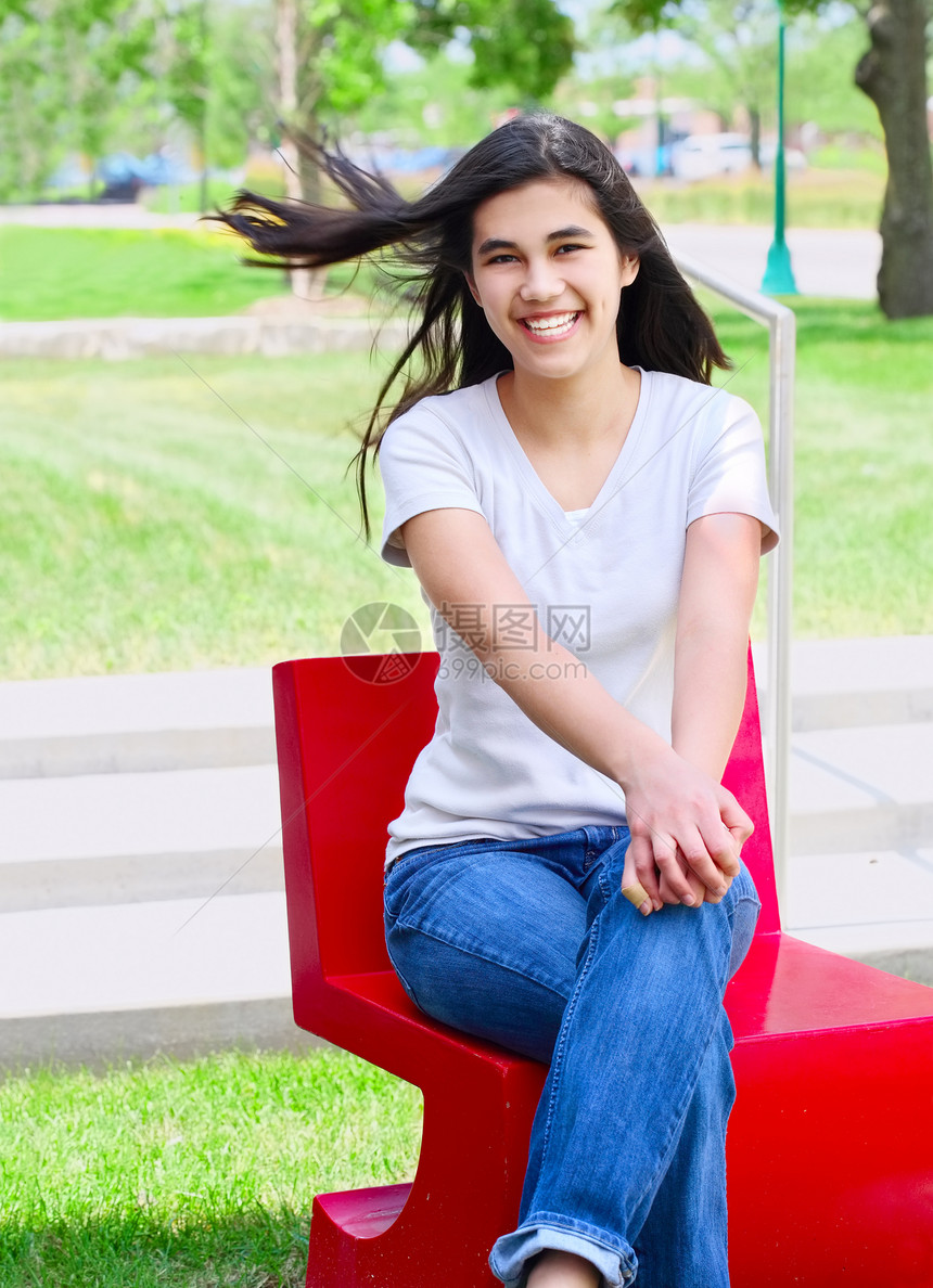 坐在红椅子上户外的美丽少女女孩混血儿微笑混血关系公园牛仔布长发青少年少数民族牛仔裤图片