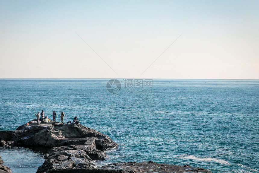 在日本海边岩石上钓鱼的人图片
