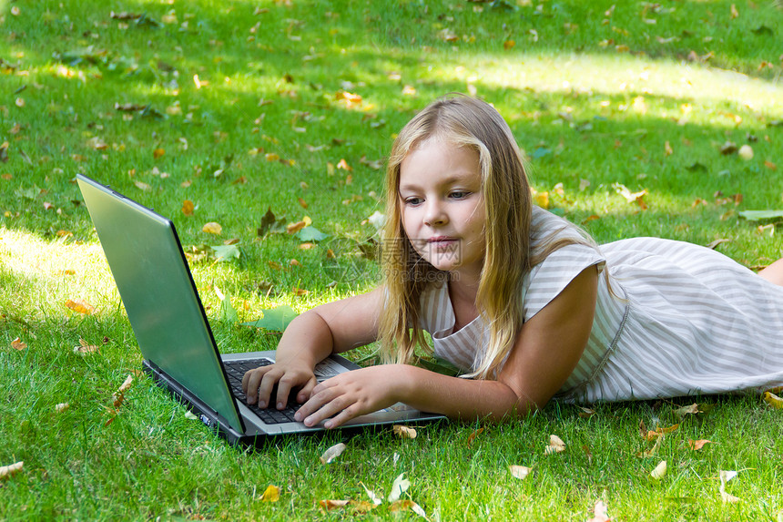 用笔记本电脑在绿草地上的可爱女孩图片