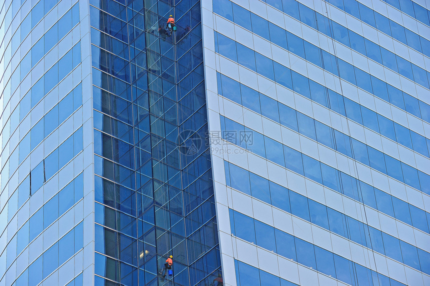 工人被悬吊在一只脚手架上 高举在蓝玻璃天窗上线条镜子工作天际摩天大楼城市反射办公室窗户商业图片
