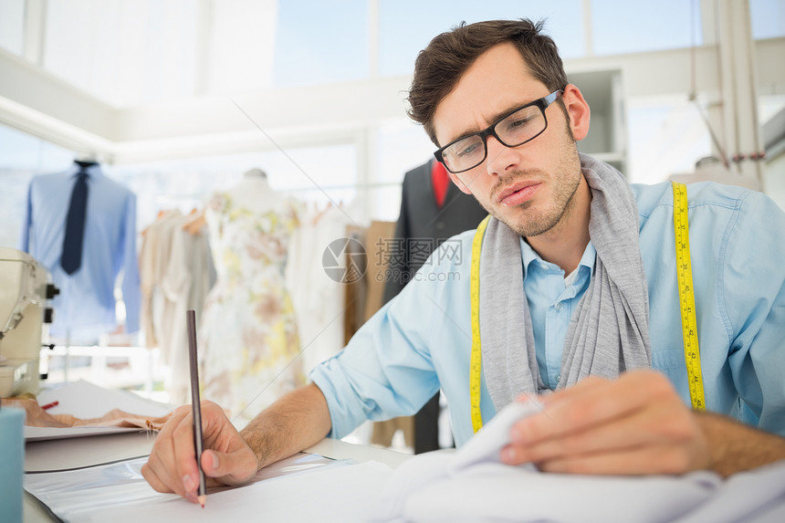 时装设计师在设计自己的设计缝纫机眼镜草图男性桌子工作工作室专注创造力造型师图片