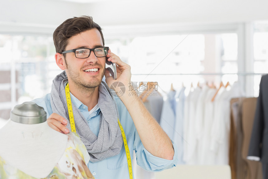 时装设计师在使用移动电话时穿衣工作剪裁男性磁带衣服爱好呼唤拨号裁缝工作室男人图片