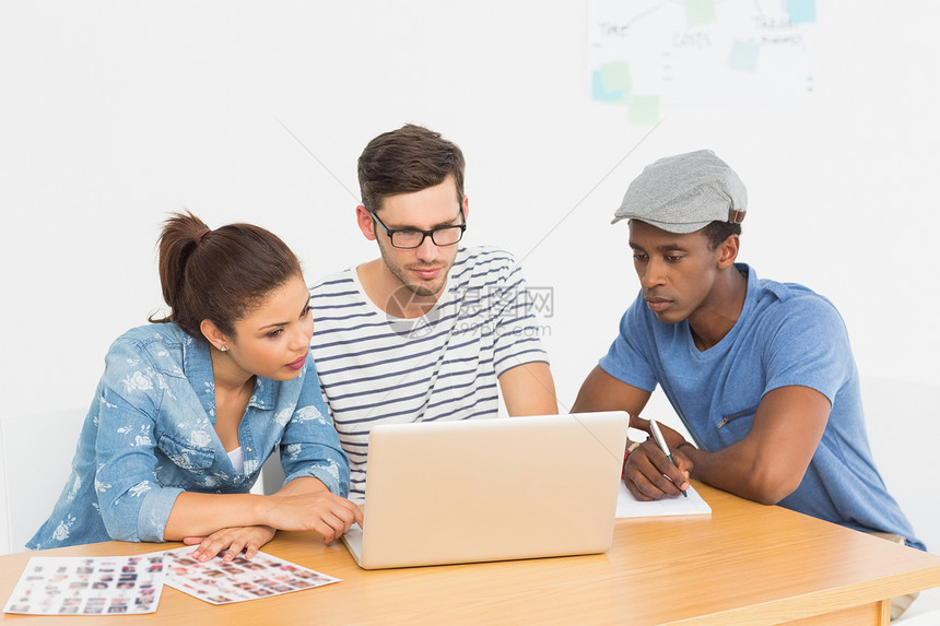 三名集中的青年艺术家在笔记本电脑上工作图片
